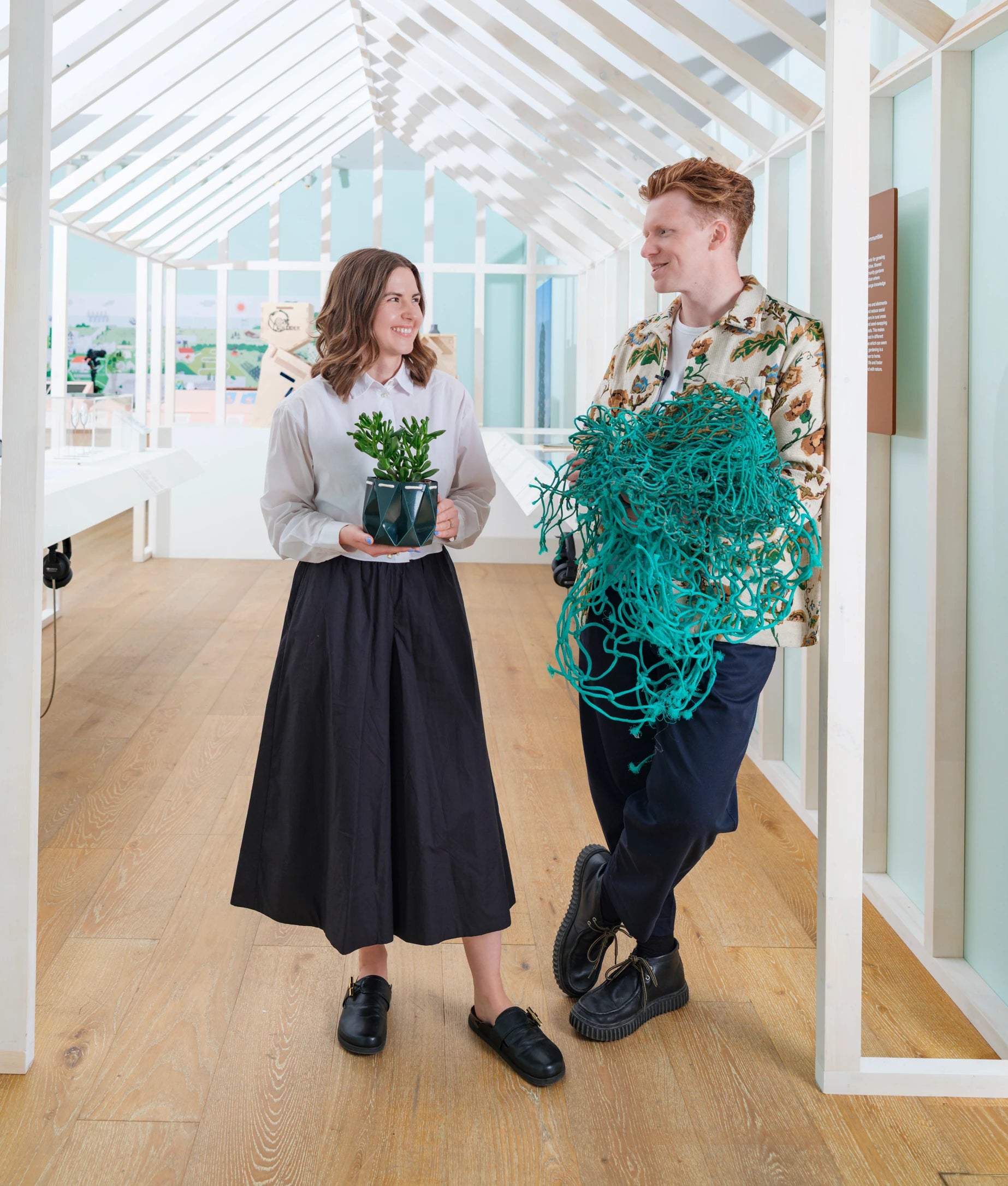 Eilidh and Andy standing in a bright studio space, holding reimagined everyday objects designed with sustainability in mind.
